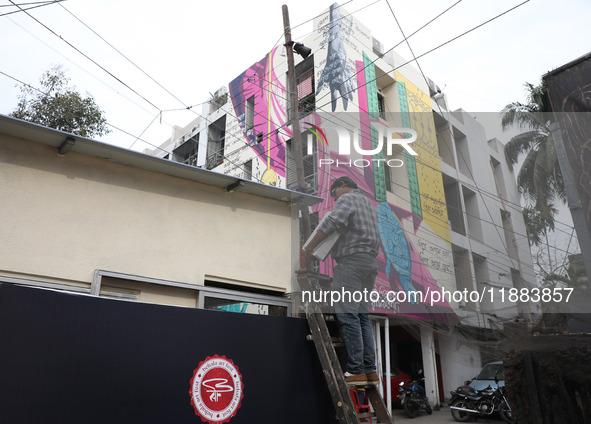 An electrician installs a light on a pole in front of a mural painted on a building during an open-air art festival, The Behala Art Fest, in...