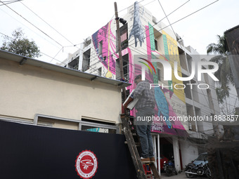 An electrician installs a light on a pole in front of a mural painted on a building during an open-air art festival, The Behala Art Fest, in...