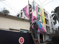 An electrician installs a light on a pole in front of a mural painted on a building during an open-air art festival, The Behala Art Fest, in...