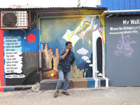 A man speaks on his mobile phone in front of a mural inside an alley during an open-air art festival, The Behala Art Fest, in Kolkata, India...