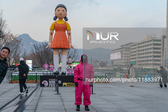 A person dressed as a ''Squid Game'' game guard stands while people take photos in front of Young-hee, a robotic doll from Netflix's ''Squid...