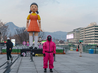 A person dressed as a ''Squid Game'' game guard stands while people take photos in front of Young-hee, a robotic doll from Netflix's ''Squid...