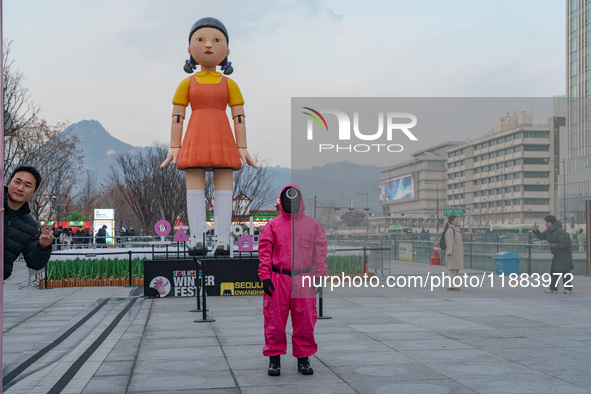 A person dressed as a ''Squid Game'' game guard stands while people take photos in front of Young-hee, a robotic doll from Netflix's ''Squid...