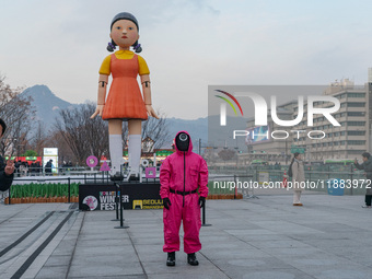 A person dressed as a ''Squid Game'' game guard stands while people take photos in front of Young-hee, a robotic doll from Netflix's ''Squid...