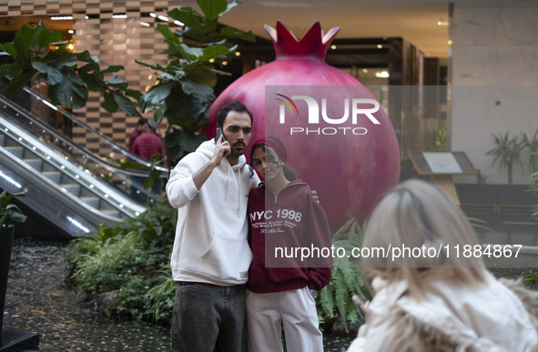 Iranian youths stand together as they pose for a photograph with a model of a pomegranate during Yalda Night celebrations at the Iran Mall s...