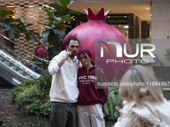 Iranian youths stand together as they pose for a photograph with a model of a pomegranate during Yalda Night celebrations at the Iran Mall s...