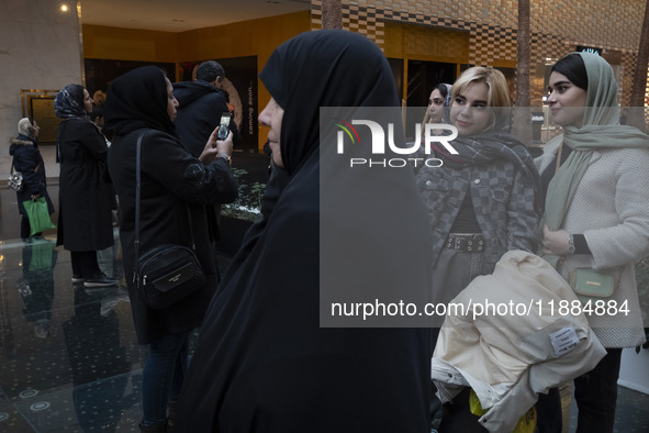 A veiled Iranian woman stands next to two young women while visiting the Iran Mall shopping mall in northwestern Tehran, Iran, on December 2...