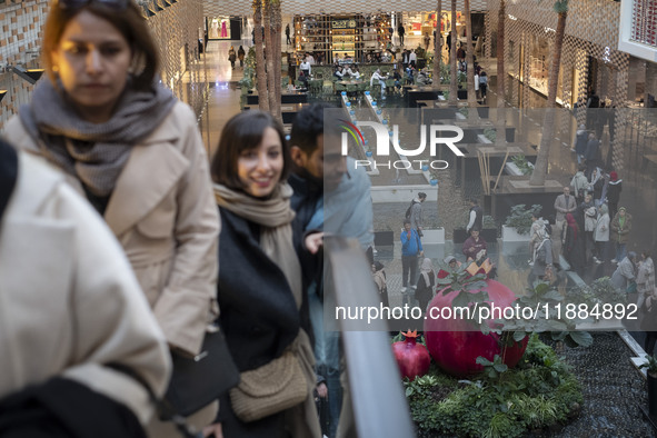 Iranian people stand next to a model of a pomegranate during Yalda Night celebrations at the Iran Mall shopping mall in northwestern Tehran,...