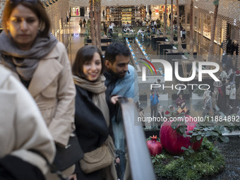 Iranian people stand next to a model of a pomegranate during Yalda Night celebrations at the Iran Mall shopping mall in northwestern Tehran,...