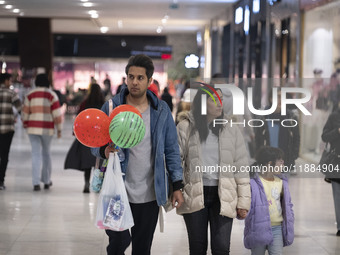 An Iranian man carries watermelon-shaped balloons as he walks with his family at the Iran Mall shopping mall in northwestern Tehran, Iran, o...