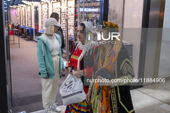 Two women wearing traditional dresses walk past a young woman during Yalda Night celebrations at the Iran Mall shopping mall in northwestern...