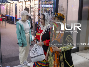 Two women wearing traditional dresses walk past a young woman during Yalda Night celebrations at the Iran Mall shopping mall in northwestern...