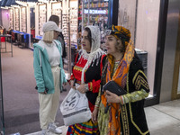 Two women wearing traditional dresses walk past a young woman during Yalda Night celebrations at the Iran Mall shopping mall in northwestern...