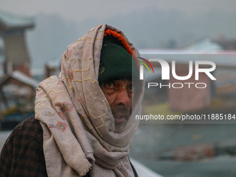 A man covers his head with a scarf as he sits on the banks of Dal Lake in Srinagar, Jammu and Kashmir, on December 21, 2024. The 40-day hars...