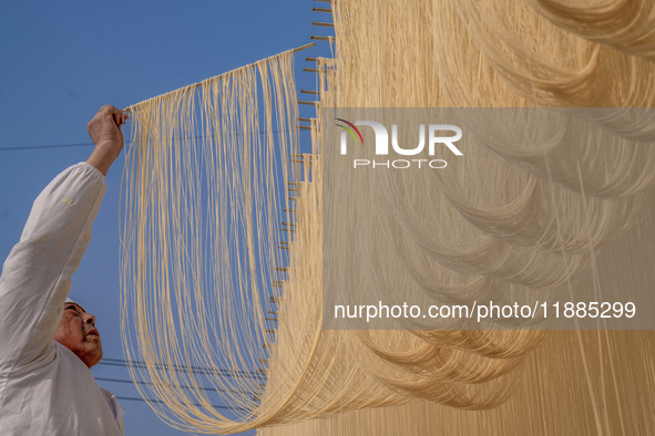 A worker places hanging noodles on a shelf to dry in Hefei, Anhui province, China, on December 21, 2024. 