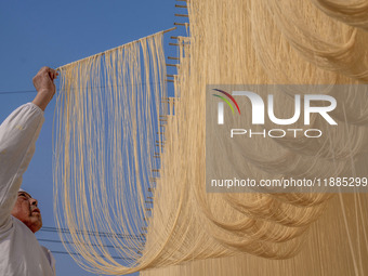 A worker places hanging noodles on a shelf to dry in Hefei, Anhui province, China, on December 21, 2024. (