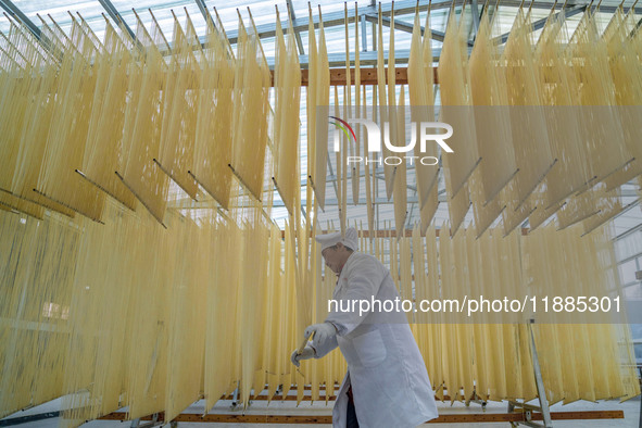 A worker places hanging noodles on a shelf to dry in Hefei, Anhui province, China, on December 21, 2024. 