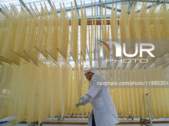 A worker places hanging noodles on a shelf to dry in Hefei, Anhui province, China, on December 21, 2024. (