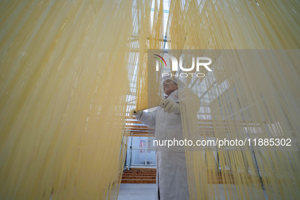 A worker places hanging noodles on a shelf to dry in Hefei, Anhui province, China, on December 21, 2024. 