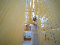 A worker places hanging noodles on a shelf to dry in Hefei, Anhui province, China, on December 21, 2024. (