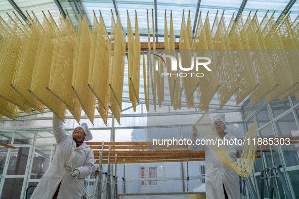 A worker places hanging noodles on a shelf to dry in Hefei, Anhui province, China, on December 21, 2024. 