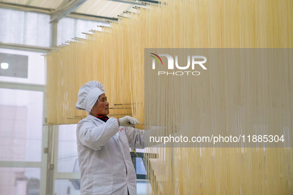 A worker places hanging noodles on a shelf to dry in Hefei, Anhui province, China, on December 21, 2024. 