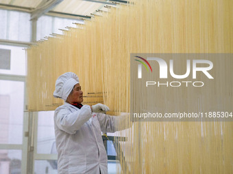 A worker places hanging noodles on a shelf to dry in Hefei, Anhui province, China, on December 21, 2024. (