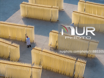 A worker places hanging noodles on a shelf to dry in Hefei, Anhui province, China, on December 21, 2024. (