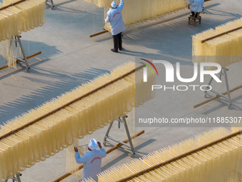 A worker places hanging noodles on a shelf to dry in Hefei, Anhui province, China, on December 21, 2024. (