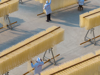 A worker places hanging noodles on a shelf to dry in Hefei, Anhui province, China, on December 21, 2024. (