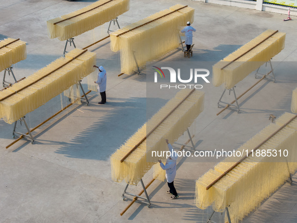 A worker places hanging noodles on a shelf to dry in Hefei, Anhui province, China, on December 21, 2024. 