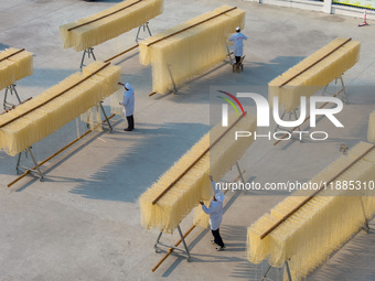 A worker places hanging noodles on a shelf to dry in Hefei, Anhui province, China, on December 21, 2024. (