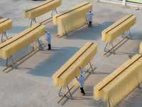 A worker places hanging noodles on a shelf to dry in Hefei, Anhui province, China, on December 21, 2024. (