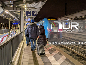 A regional train and passengers with luggage are on a platform at Munich Pasing station in Munich, Bavaria, Germany, on December 20, 2024. (