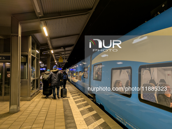 A regional train and passengers with luggage are on a platform at Munich Pasing station in Munich, Bavaria, Germany, on December 20, 2024. 