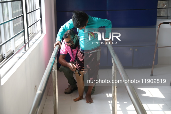 A worker assists as a boy attempts to walk using a railing for support after acquiring a new prosthetic limb inside the Rehabilitation & Res...