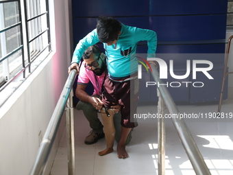 A worker assists as a boy attempts to walk using a railing for support after acquiring a new prosthetic limb inside the Rehabilitation & Res...