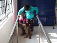 A worker assists as a boy attempts to walk using a railing for support after acquiring a new prosthetic limb inside the Rehabilitation & Res...