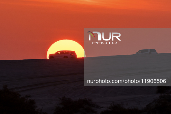 Tourists drive a car along the Sealine Sand Dunes against the backdrop of the last sunset of the year 2024 in Sealine, Qatar, on December 31...