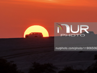 Tourists drive a car along the Sealine Sand Dunes against the backdrop of the last sunset of the year 2024 in Sealine, Qatar, on December 31...