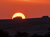 Tourists drive a car along the Sealine Sand Dunes against the backdrop of the last sunset of the year 2024 in Sealine, Qatar, on December 31...