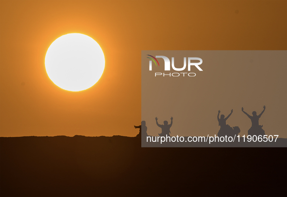 People ride on a camel along the Sealine Sand Dunes against the backdrop of the last sunset of the year 2024 in Sealine, Qatar, on December...