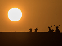 People ride on a camel along the Sealine Sand Dunes against the backdrop of the last sunset of the year 2024 in Sealine, Qatar, on December...