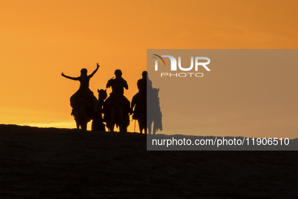 People ride on a camel along the Sealine Sand Dunes against the backdrop of the last sunset of the year 2024 in Sealine, Qatar, on December...