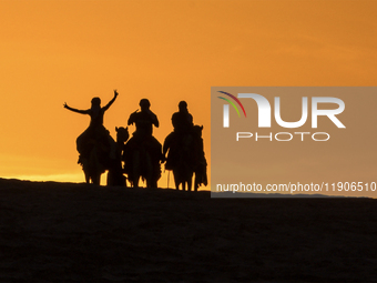 People ride on a camel along the Sealine Sand Dunes against the backdrop of the last sunset of the year 2024 in Sealine, Qatar, on December...