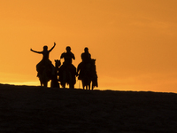 People ride on a camel along the Sealine Sand Dunes against the backdrop of the last sunset of the year 2024 in Sealine, Qatar, on December...