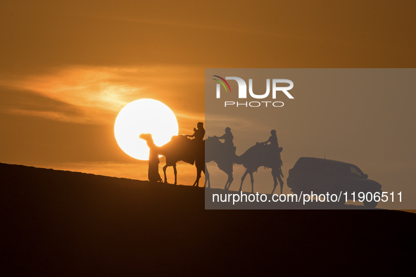 People ride on a camel along the Sealine Sand Dunes against the backdrop of the last sunset of the year 2024 in Sealine, Qatar, on December...