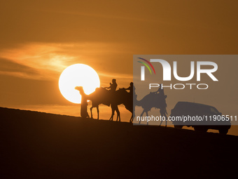 People ride on a camel along the Sealine Sand Dunes against the backdrop of the last sunset of the year 2024 in Sealine, Qatar, on December...