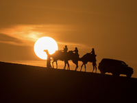 People ride on a camel along the Sealine Sand Dunes against the backdrop of the last sunset of the year 2024 in Sealine, Qatar, on December...