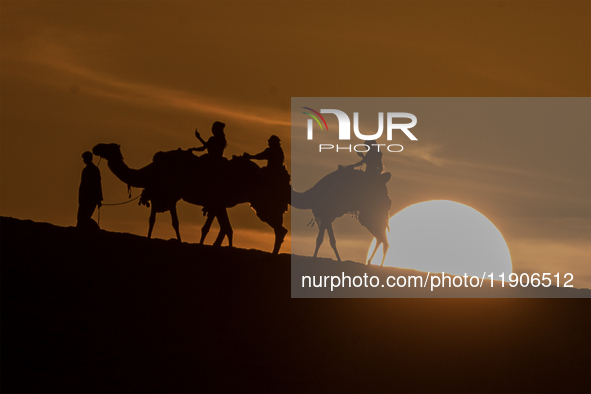 People ride on a camel along the Sealine Sand Dunes against the backdrop of the last sunset of the year 2024 in Sealine, Qatar, on December...